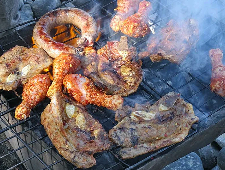 Vlees, worst en kippenpoten op de grill boven open vuur