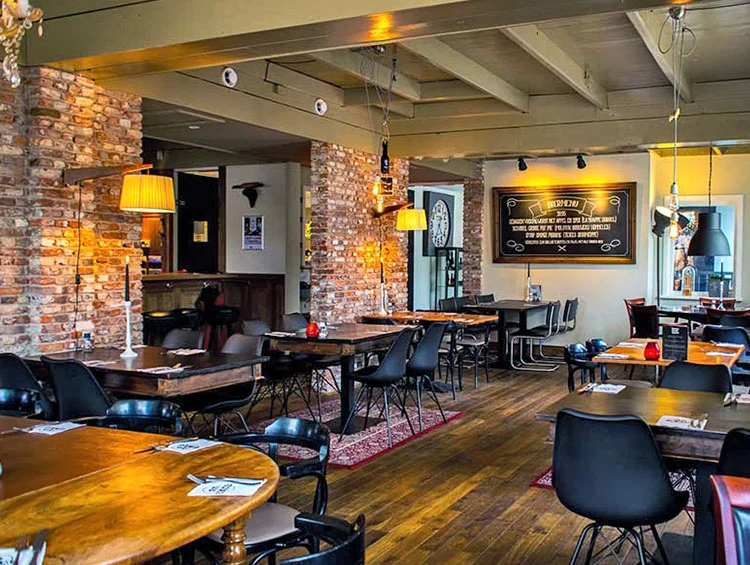 Restaurantzaal met bakstenen muren, houten tafels en een menubord aan de wand