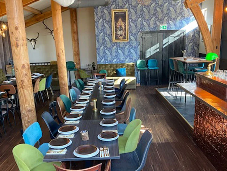 Lange gedekte tafel in zaal Yonkers, met pauwenbehang en de bar met groene lamp