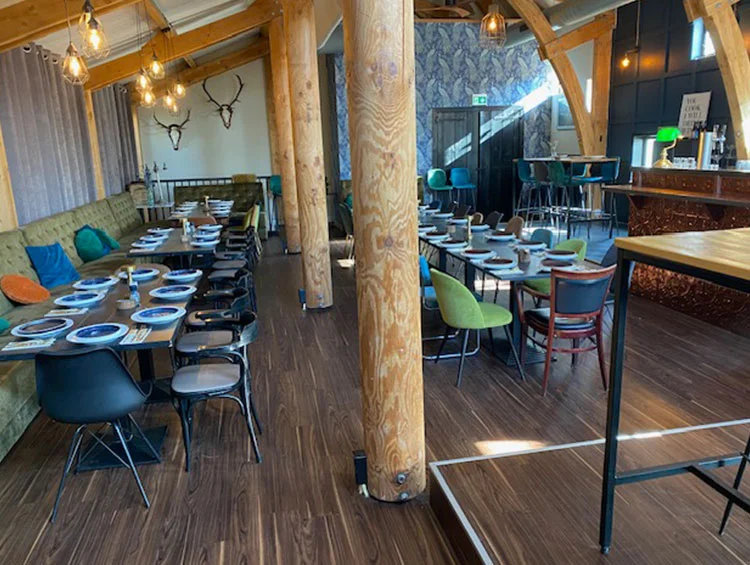 Zaal Yonkers met houten pilaren, gedekte tafels langs de bank en de bar achterin