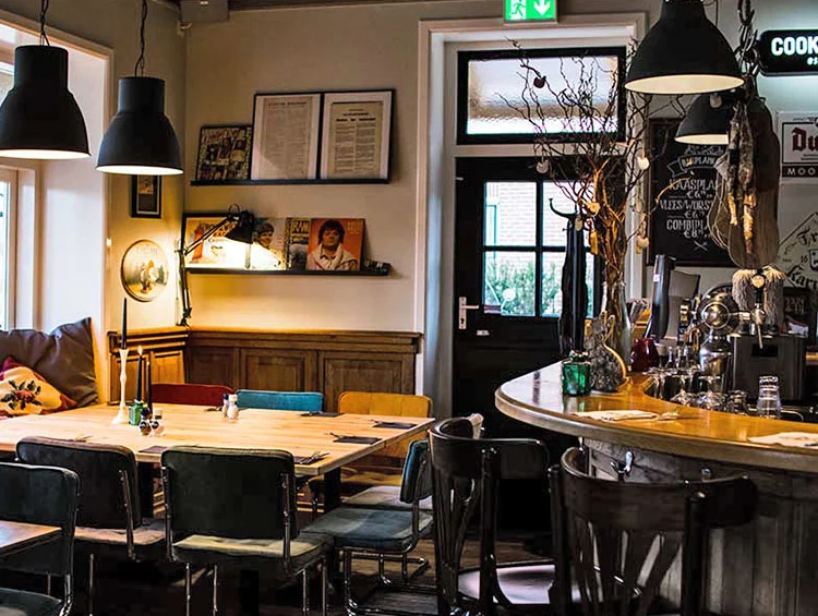 Lange houten tafel bij de bar, met hanglampen en platen aan de muur